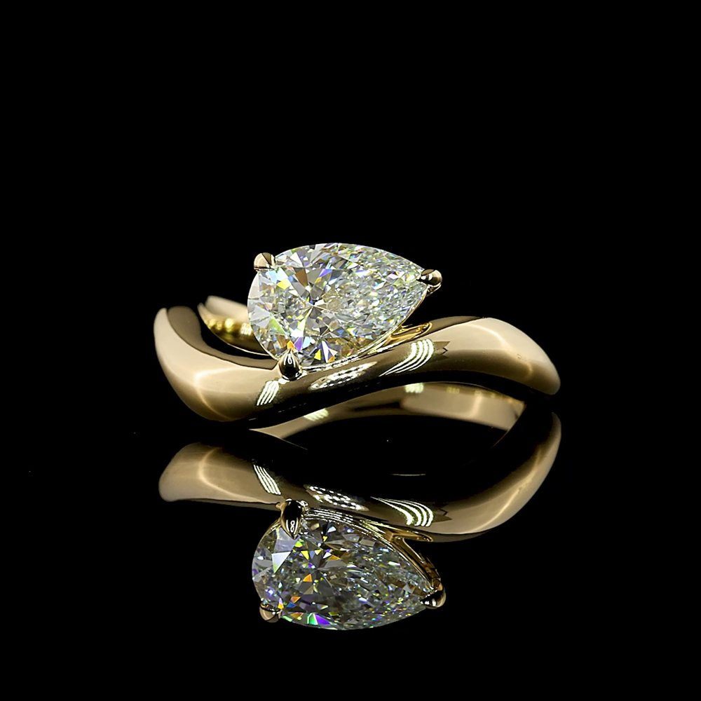 A pear-shaped diamond set east-west in a sculptural yellow gold bypass ring