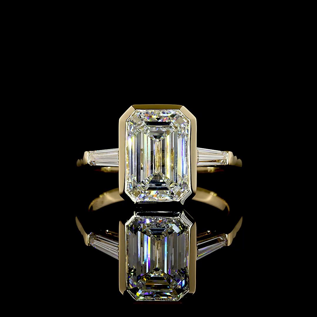A bezel-set emerald-cut diamond with tapered baguette side stones in yellow gold