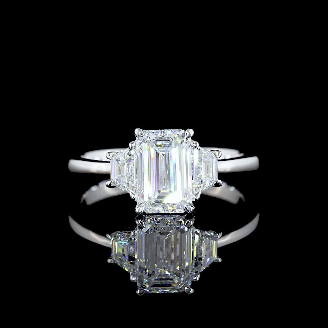 An emerald-cut diamond flanked by two trapezoid side stones in a platinum three-stone ring